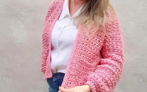 Mujer con un cardigan a crochet rosa, sobre una camisa blanca y jeans.
