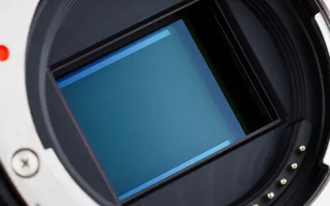 Zbliżenie na matrycę CMOS aparatu fotograficznego. Błękitna powierzchnia czujnika otoczona jest czarną ramką i metalowym pierścieniem z pinami.