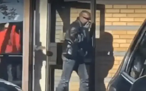 Kanye West i Sverige, klädd i läderjacka och solglasögon, lämnar en byggnad.