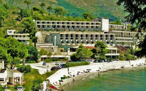 Opuszczone hotele Chorwacja, zniszczone budynki hotelowe na wzgórzu, plaża z ludźmi i morze.