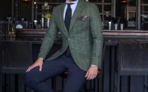 Elegancki mężczyzna w marynarce w kratę (butelkowa zieleń) i granatowych spodniach. W tle bar z elementami pudrowego różu.