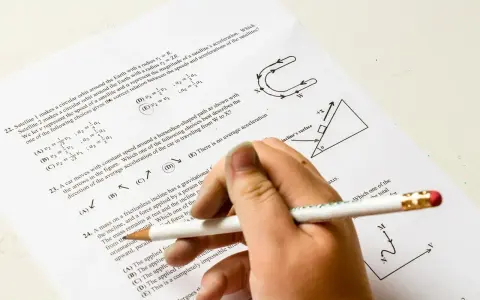 Ręka z ołówkiem rozwiązuje test fizyczny. Pytanie 22 dotyczy satelitów, a pytanie 23 ruchu po torze w kształcie podkowy. Od ilu procent jest 5?