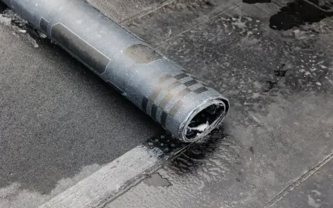 Rolka papy na zimno leży na mokrym dachu. Widać fragmenty czarnej papy i charakterystyczny wzór na rolce.