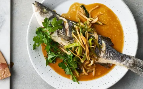 Ein ganzer Wolfsbarsch Fisch, gedünstet in einer würzigen Sauce mit Ingwer und Frühlingszwiebeln, garniert mit Koriander.