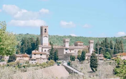 La Badia a Passignano, un borgo medievale toscano con un'imponente torre dell'orologio, circondato da colline verdi e cipressi.