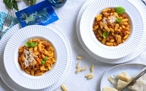 Due piatti di gnocchetti alla campidanese, un assaggio di Sardegna con sugo di salsiccia e pomodoro, guarniti con basilico e parmigiano.