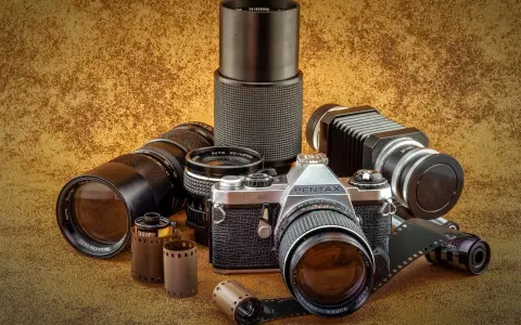 Kolekcja sprzętu fotograficznego: aparat Pentax JMC Super, obiektywy, mieszek i klisze.