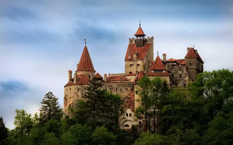Zamek Bran w Rumunii, otoczony zielenią, z charakterystycznymi wieżami i czerwonymi dachami, wygląda jak z bajki.