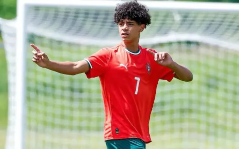 Cristiano Ronaldo Jr. con pelo rizado y camiseta roja con el número 7, señalando con el dedo índice.