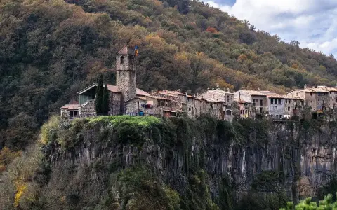 Castellfollit de la Roca, un pueblo medieval colgado sobre un acantilado basáltico, se alza majestuoso entre bosques otoñales.