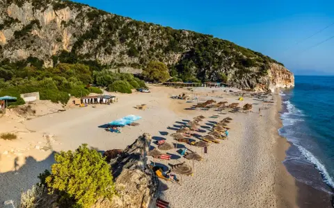 Piękne albania plaże z rzędami parasoli i leżaków, skaliste zbocze i turkusowe morze.