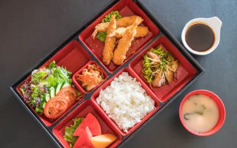 Japoński obiad w bento: smażone krewetki, ryż, sałatka, owoce i zupa miso.