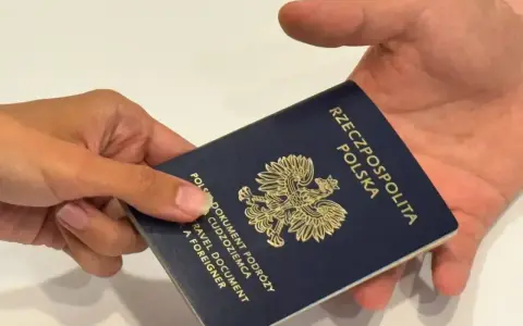 Dłoń przekazuje ciemnoniebieski paszport polski z godłem orła. Dokument podróży gotowy do przekroczenia granicy.