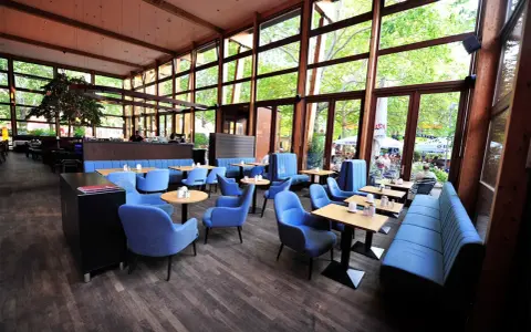 Gemütliches **Cafe Wilmersdorf** mit blauen Sesseln und Bänken, Holzboden und großen Fenstern, die auf eine grüne Terrasse blicken.