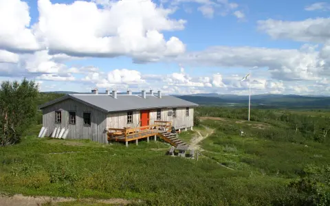 Kungsleden stugor i fjällandskap med molnig himmel. Enkel träbyggnad med veranda och flaggstång.