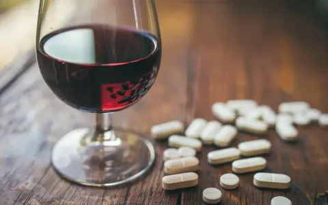 Kieliszek czerwonego wina obok garści tabletek. Leki przeciwzapalne a alkohol – potencjalne ryzyko interakcji.