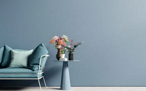 Divano blu petrolio e cuscini in tonalità pastello su sfondo azzurro polvere. Ottime idee colori pareti per un ambiente rilassante.