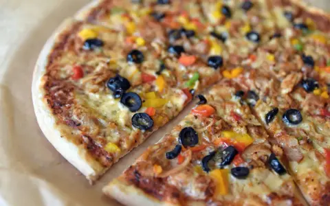 Co to jest pizza? To pyszna, okrągła pizza z oliwkami, papryką i serem, pokrojona na kawałki.