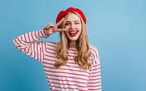 Mujer con boina roja y camiseta a rayas, haciendo el signo de la paz, con un estilo que evoca un caracter francés.