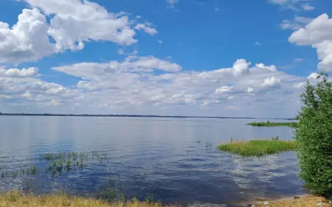 Spokojny zalew Jeziorsko w letni dzień. Błękitne niebo z białymi chmurami odbija się w tafli wody.