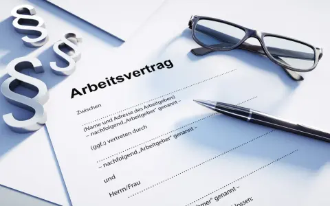 Drei Paragraphen-Symbole, eine Brille und ein Stift liegen auf einem Dokument mit der Überschrift "Arbeitsvertrag". Dies unterstreicht, dass ein Arbeitsvertrag schriftlich sein muss.