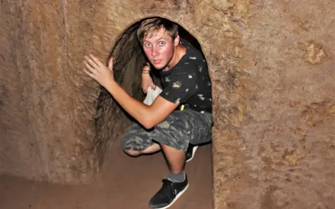 Młody mężczyzna kuca w wąskim tunelu, jednym z historycznych Cu Chi Tunnels.