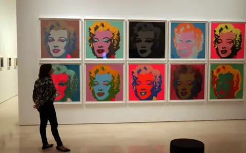 Una persona observa la icónica serie de Marilyn de Andy Warhol, con retratos vibrantes en colores pop.