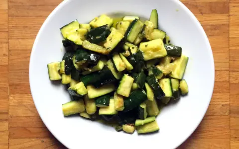Zucchine in umido, un contorno saporito e leggero, servito in un piatto bianco su un tagliere di legno.