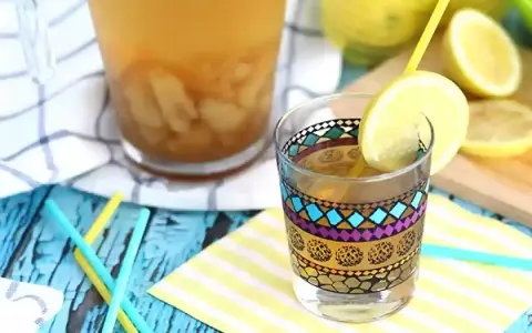Ett glas med en färgglad dekorativ kant, fyllt med iste och en citronskiva. Bredvid står en karaff med iste och färska citroner. Perfekt iste recept för en varm dag.