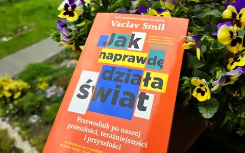 Książka Vaclava Smila "Jak naprawdę działa świat" wśród kwiatów. To przewodnik po przeszłości, teraźniejszości i przyszłości, który pomaga zrozumieć, co to odwyk od błędnych przekonań.