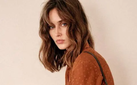 Mujer con un corte de pelo clavicut, ondas suaves y flequillo desfilado, luciendo un top marrón con lunares.