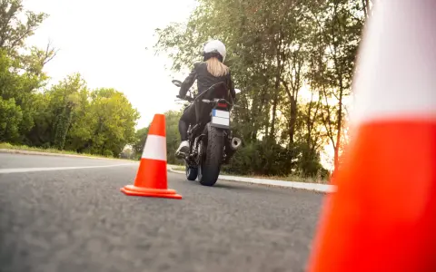 Kobieta na motocyklu podczas egzaminu na prawo jazdy kat A. Sprawdza cenę kursu.