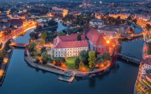 Ostrów Tumski we Wrocławiu nocą, z oświetlonymi budynkami i rzeką. To jedno z najpiękniejszych miejsc Wrocławia.