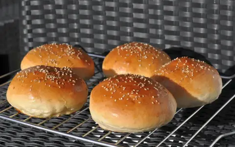 Fünf goldbraune Burgerbrötchen mit Sesam, perfekt für ein Burgerbrötchen-Rezept.