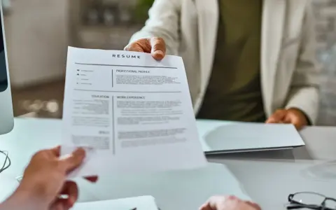Osoba w jasnej marynarce podaje dokument CV.