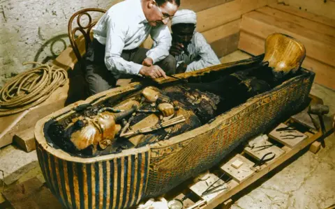 La photo découverte tombeau Toutankhamon : des archéologues examinent la momie dans son sarcophage orné.