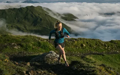 Donna corre su sentiero montano, immersa nella nebbia. Il trail running significato è libertà e sfida.