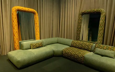 Salon w stylu vintage: zielona, modułowa kanapa i dwa lustra w ozdobnych, żółto-zielonych ramach.