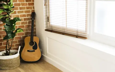 Gitara akustyczna obok ceglanej ściany i rośliny w koszu. Idealne miejsce na naukę piosenki na gitarę dla początkujących dzieci.