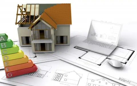 Maquette de maison, échelle d'énergie, plans et ordinateur portable. L'isolation RGE Qualibat est essentielle pour une maison performante.