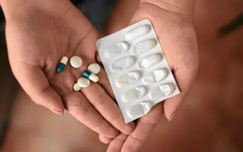Dłonie trzymające tabletki i blister. Wśród nich są leki, które mogą być inhibitorami pompy protonowej, pomagając w leczeniu dolegliwości żołądkowych.