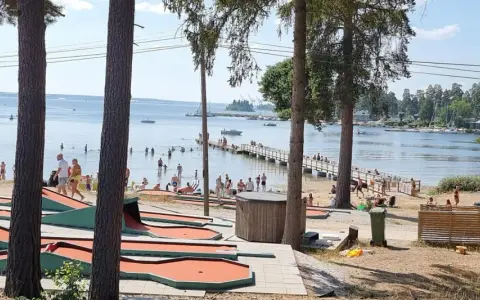 Minigolfbana vid Engesbergs camping. Många badar och solar vid vattnet, en brygga leder ut i sjön.