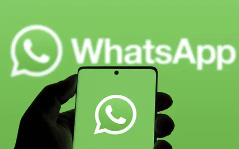 Hand hält Smartphone mit WhatsApp-Logo vor grünem Hintergrund.