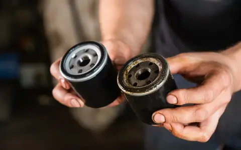 Nowy i zużyty filtr oleju w dłoniach mechanika. Wymiana filtra oleju to kluczowy element dbania o silnik.