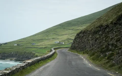A winding road along the coast of Ireland, perfect for renting a car and exploring the dramatic green hills and stone walls.