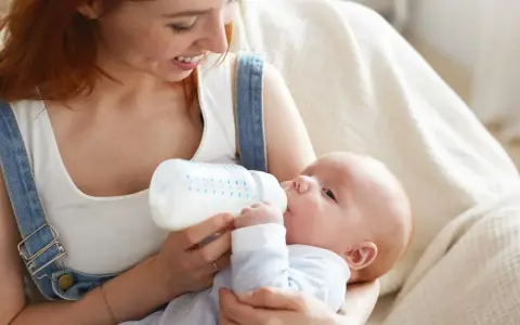 Mamma con capelli rossi nutre il suo neonato con latte artificiale ogni 2 ore. Il piccolo beve con gusto dalla bottiglia.