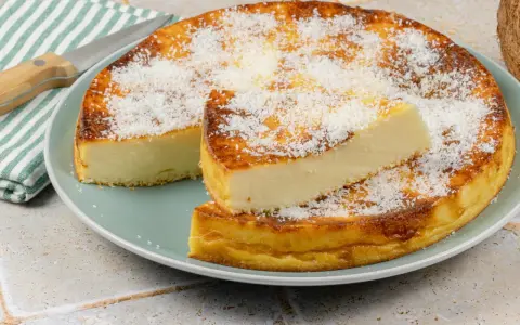 Un délicieux flan coco, saupoudré de noix de coco râpée, est servi sur une assiette. Une part est coupée et posée sur le dessus.