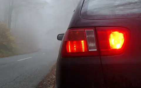Czerwone światła stopu i włączone przeciwmgielne przednie samochodu na mglistej drodze w lesie.