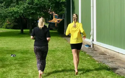 Två kvinnor njuter av en löprunda barfota på gräset en solig dag.