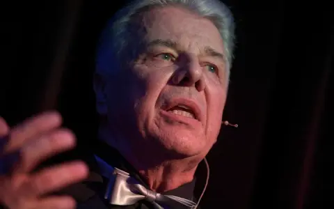 Emilian Kamiński, znany z wielu filmów, w eleganckim stroju z muszką, przemawia na scenie.